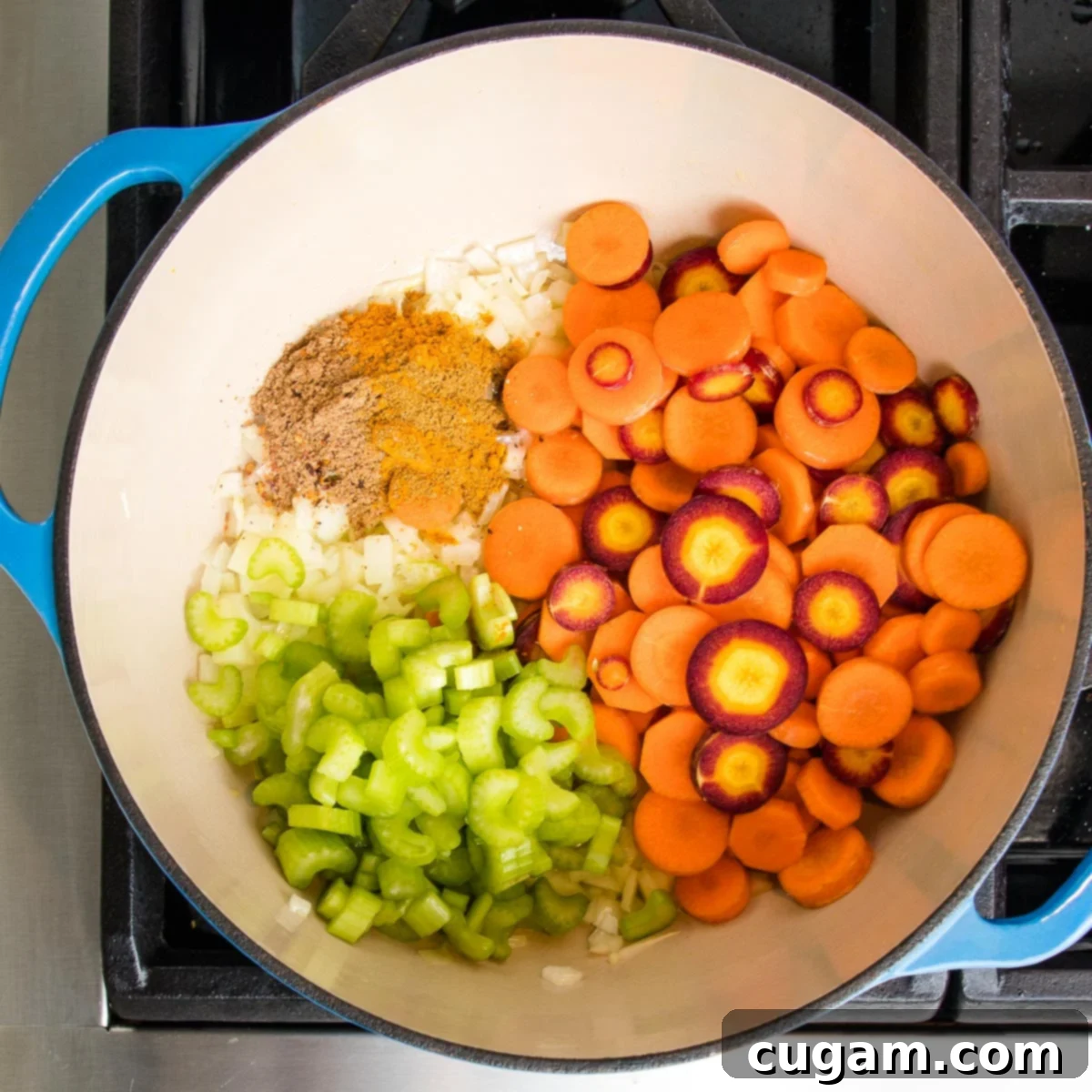 Dutch oven with layers of vegetables cooking. You can see purple and orange sliced carrots, sliced celery, some onions and a bunch of spices.