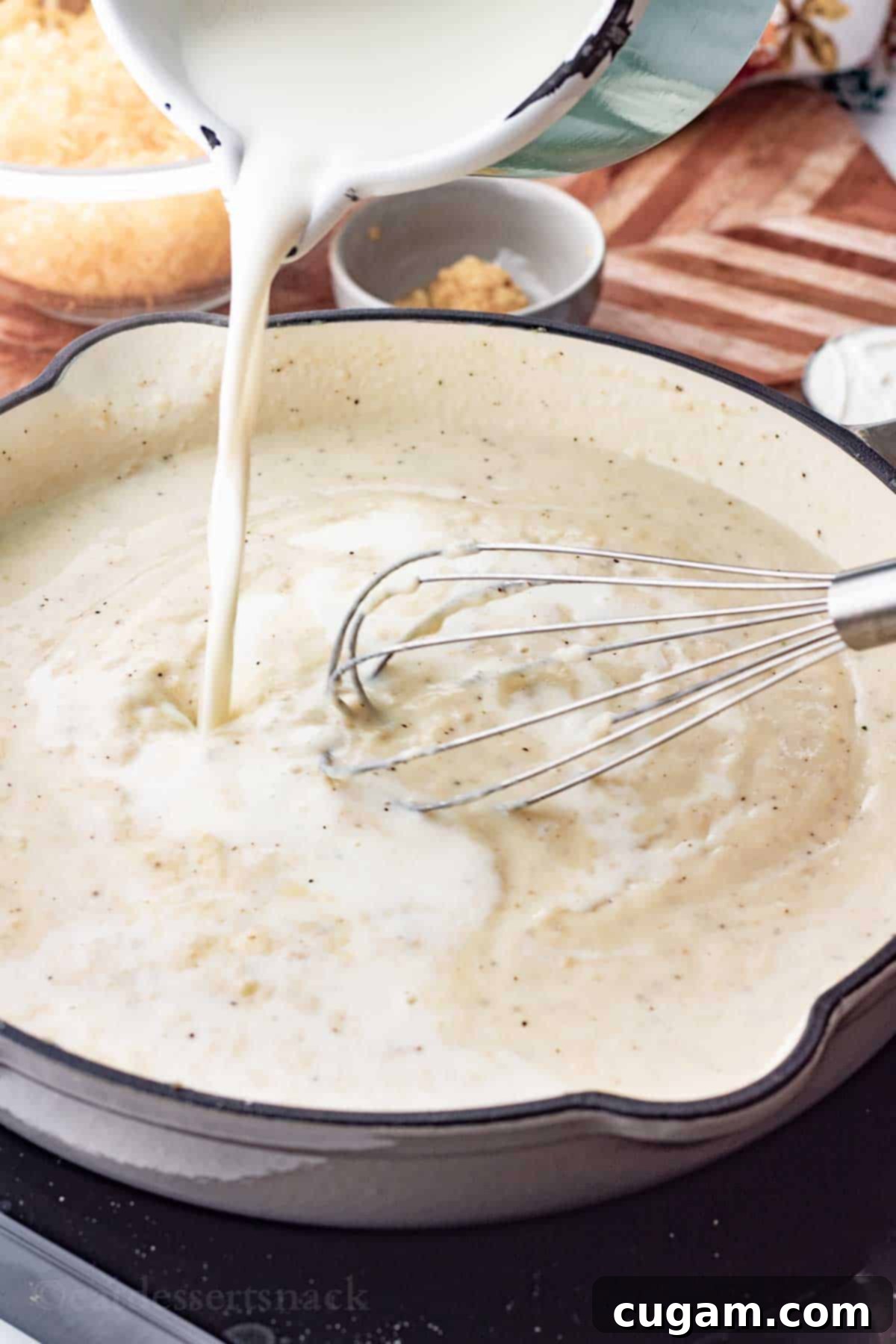 Whole milk pouring from a pristine pitcher into a large frying pan, being skillfully whisked into a creamy flour and spice mixture.
