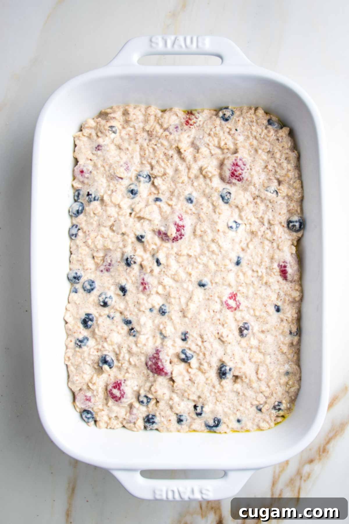 A pristine white baking dish, specifically a 2-quart casserole dish, evenly filled with the prepared berry and oatmeal mixture, spread out smoothly.