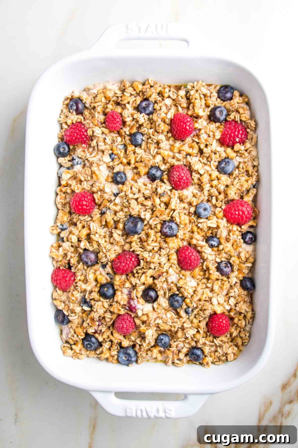 The casserole dish showcasing the oatmeal mixture, topped with the crunchy nut and oat topping, and then embellished with a final sprinkle of fresh, colorful berries for a beautiful presentation.