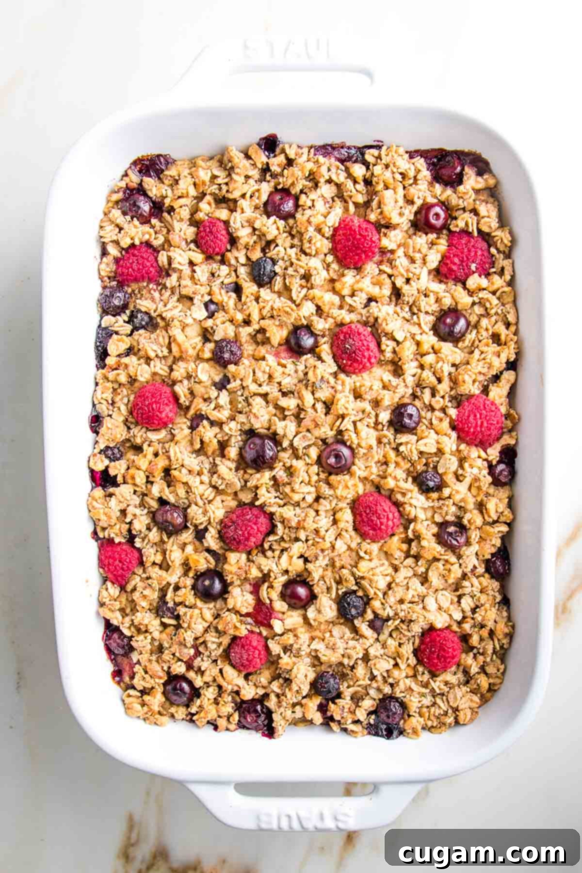 The fully assembled baked oatmeal, adorned with berries, sits in its casserole dish, ready to be placed into the oven.