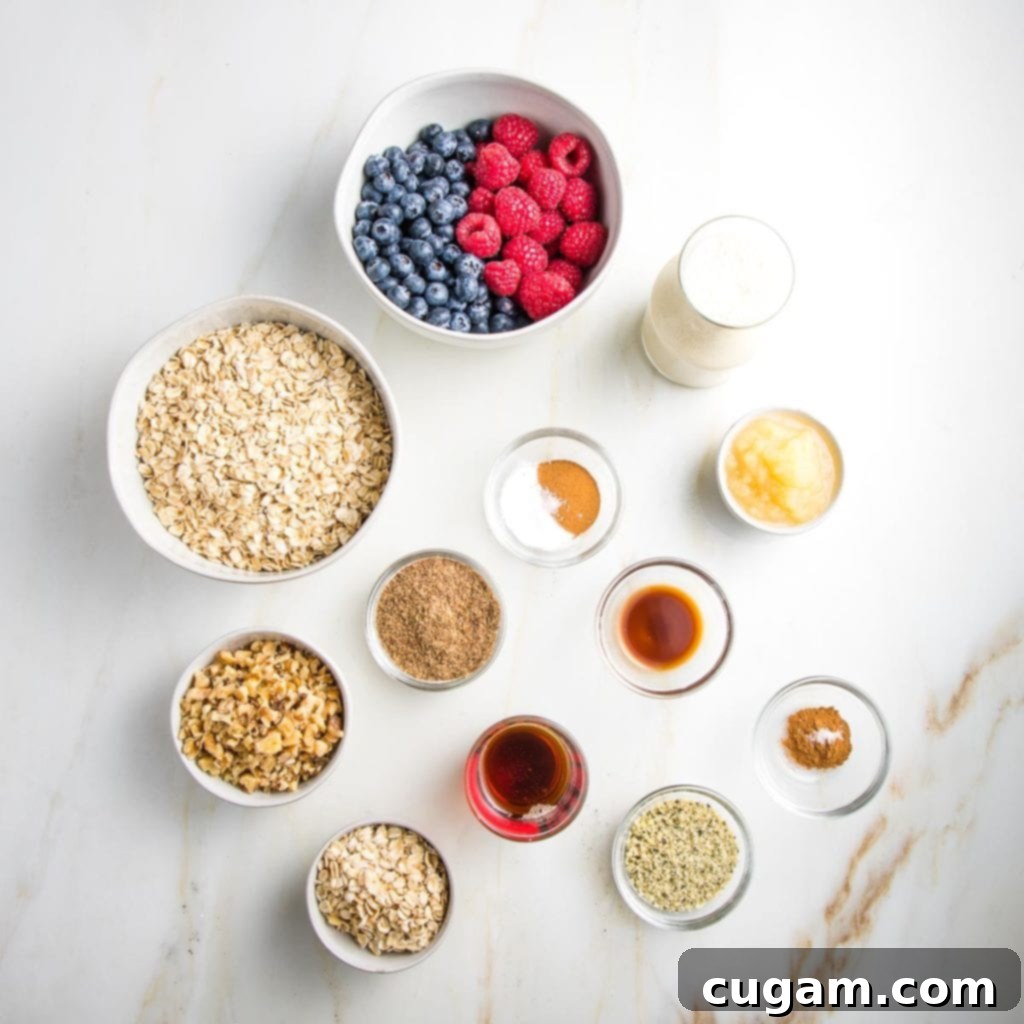 A flat lay of fresh ingredients laid out on a white surface, including a bowl of old-fashioned oats, a carton of almond milk, a jar of applesauce, a container of fresh mixed berries (raspberries, blueberries), a small bowl of ground flaxseed, cinnamon sticks, vanilla extract, and walnuts.