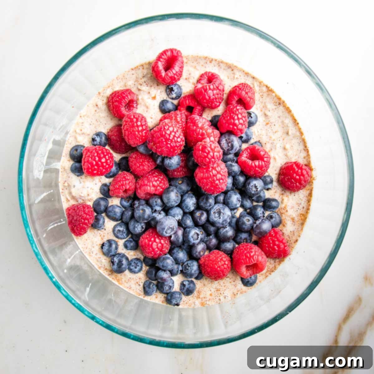 A vibrant mix of fresh blueberries and raspberries scattered over the surface of the prepared oatmeal mixture in a bowl.