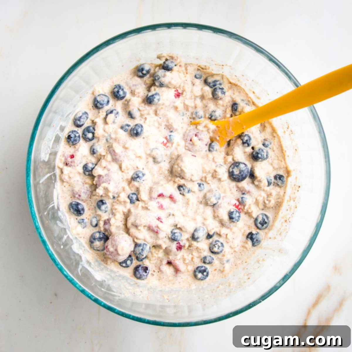Assorted berries, including blueberries and raspberries, carefully mixed into the oat mixture, ensuring they remain mostly whole and evenly distributed.