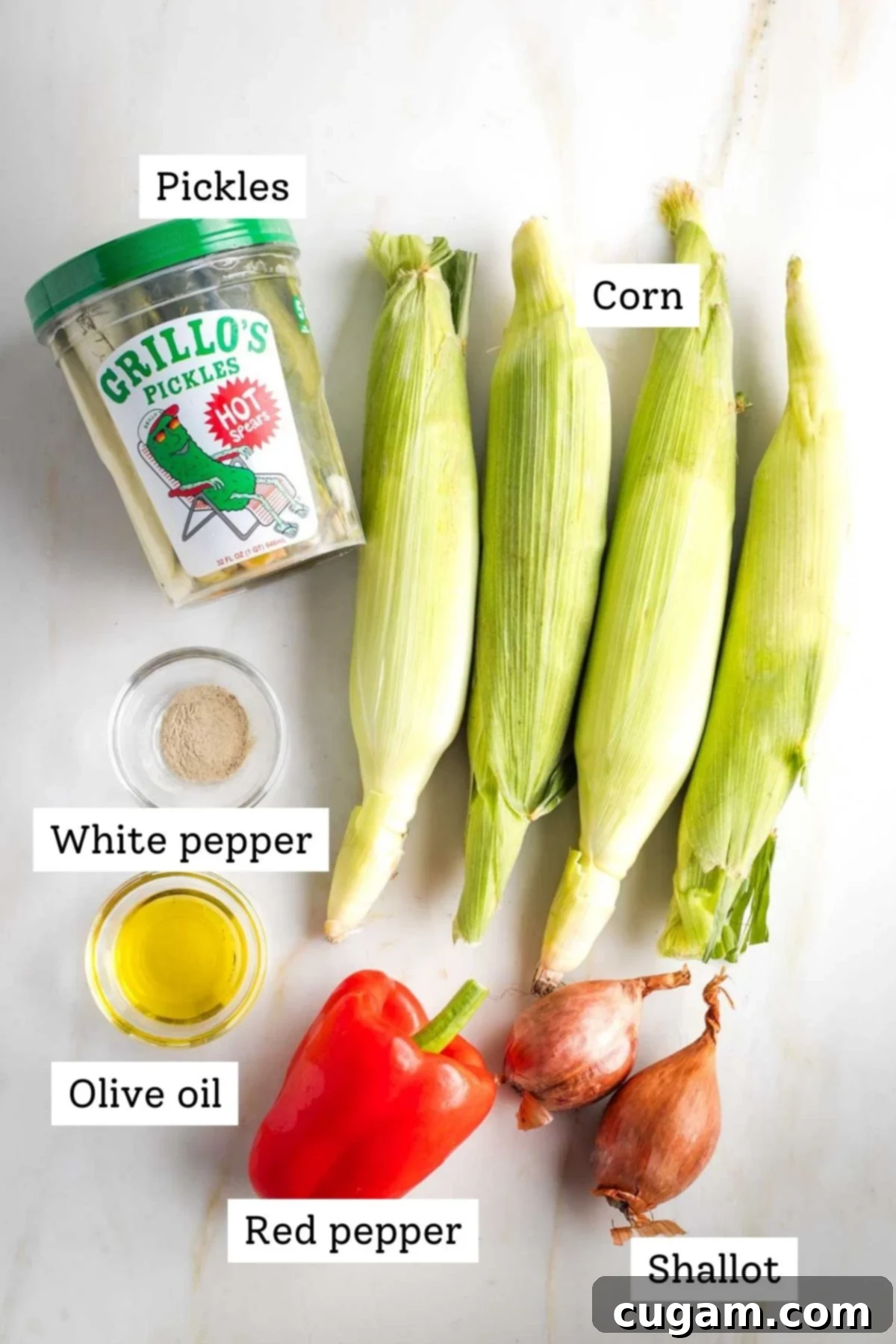 Israeli Corn and Pickle Salad 3 Individual ingredients for Israeli Corn Salad laid out on a surface, clearly labeled: pickles, corn kernels, white pepper, olive oil, diced red pepper, and shallots.