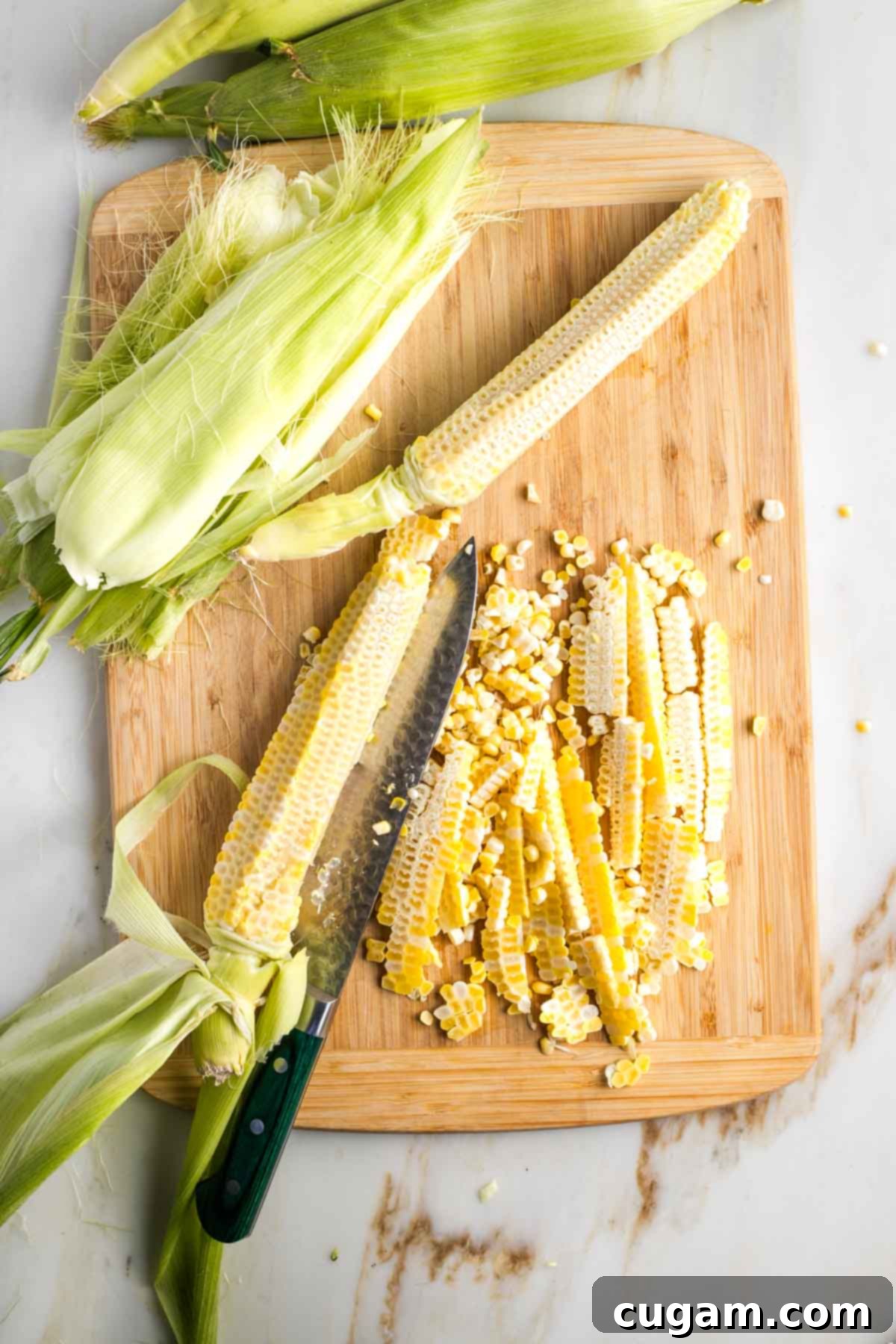 Israeli Corn and Pickle Salad 6 Three stripped corn cobs, now bare of kernels, lying on a cutting board next to a pile of fresh corn kernels, demonstrating the result of cutting corn off the cob.