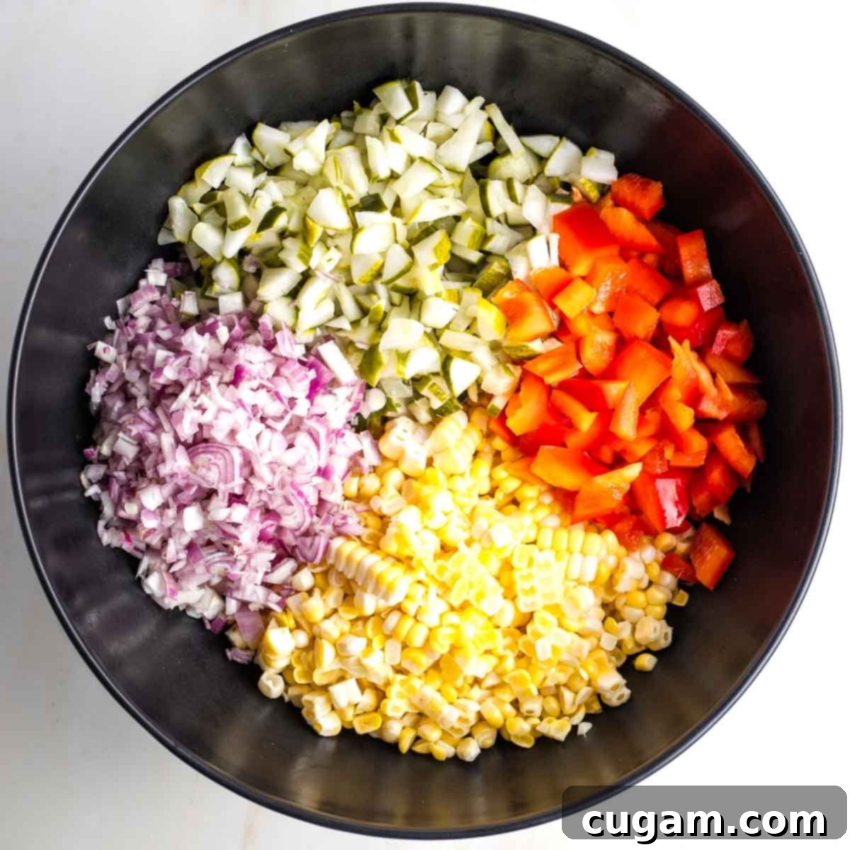 Israeli Corn and Pickle Salad 9 A large black mixing bowl filled with distinctly separated sections of colorful, freshly diced ingredients: yellow corn, green and red pickles, purple shallots, and red bell peppers.