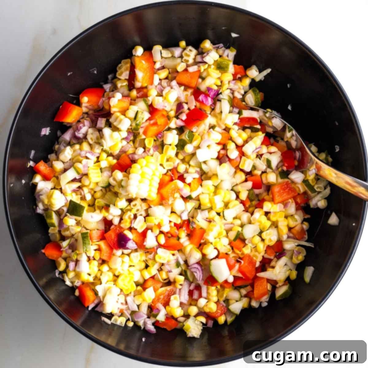 Israeli Corn and Pickle Salad 10 A close-up of a colorful Israeli corn and pickle salad, with red peppers and shallots visible, expertly mixed and glistening with olive oil, in a large black bowl.