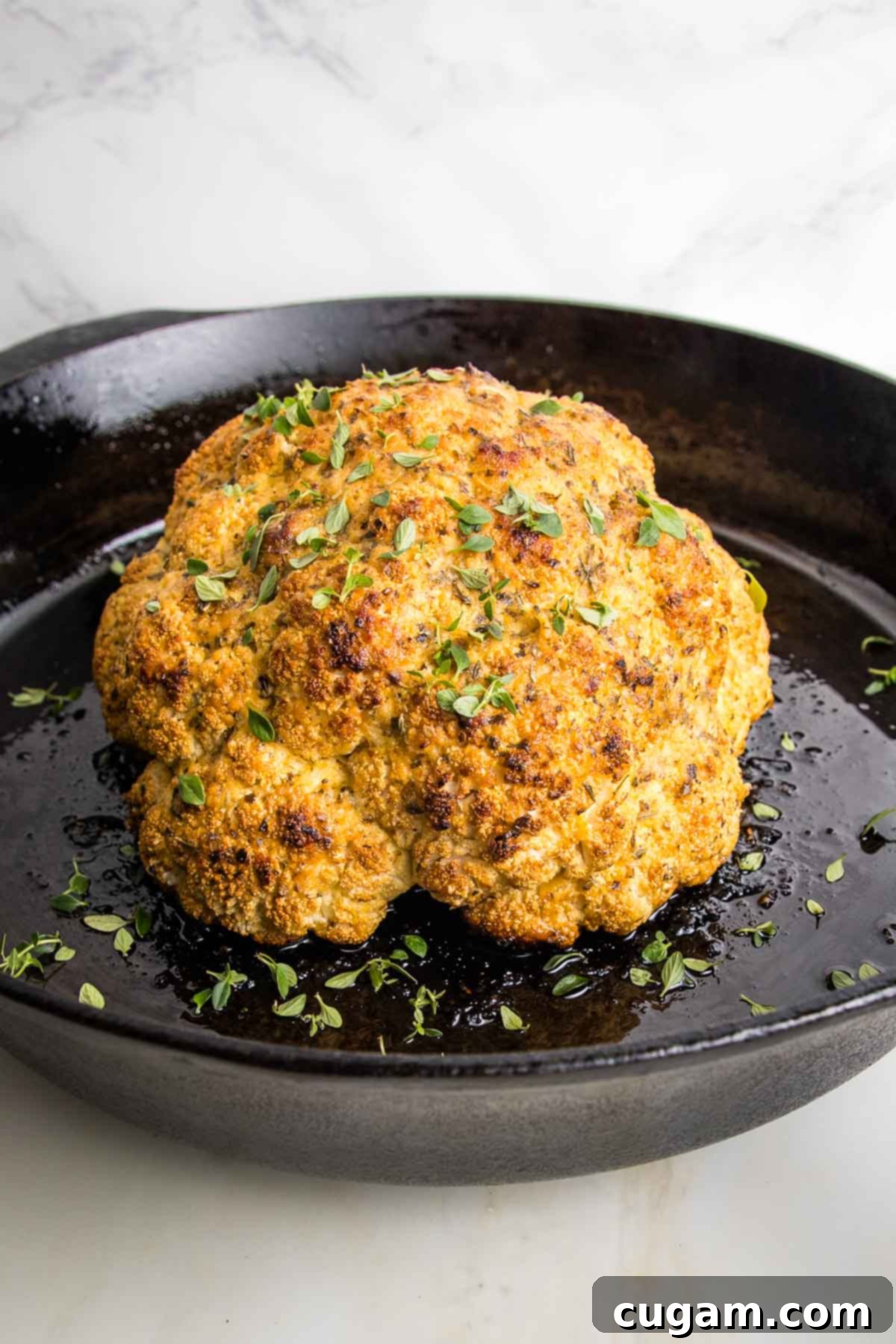 whole roasted cauliflower in a cast iron skillet, sprinkled with fresh herbs