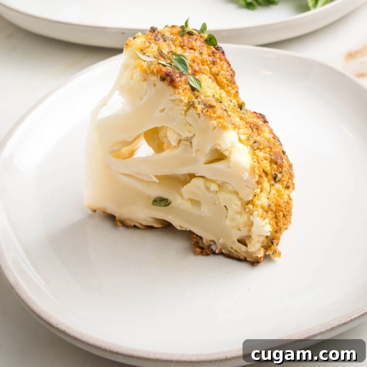 A wedge of a whole roasted cauliflower on a white plate. Golden on the outside, tender on the inside.
