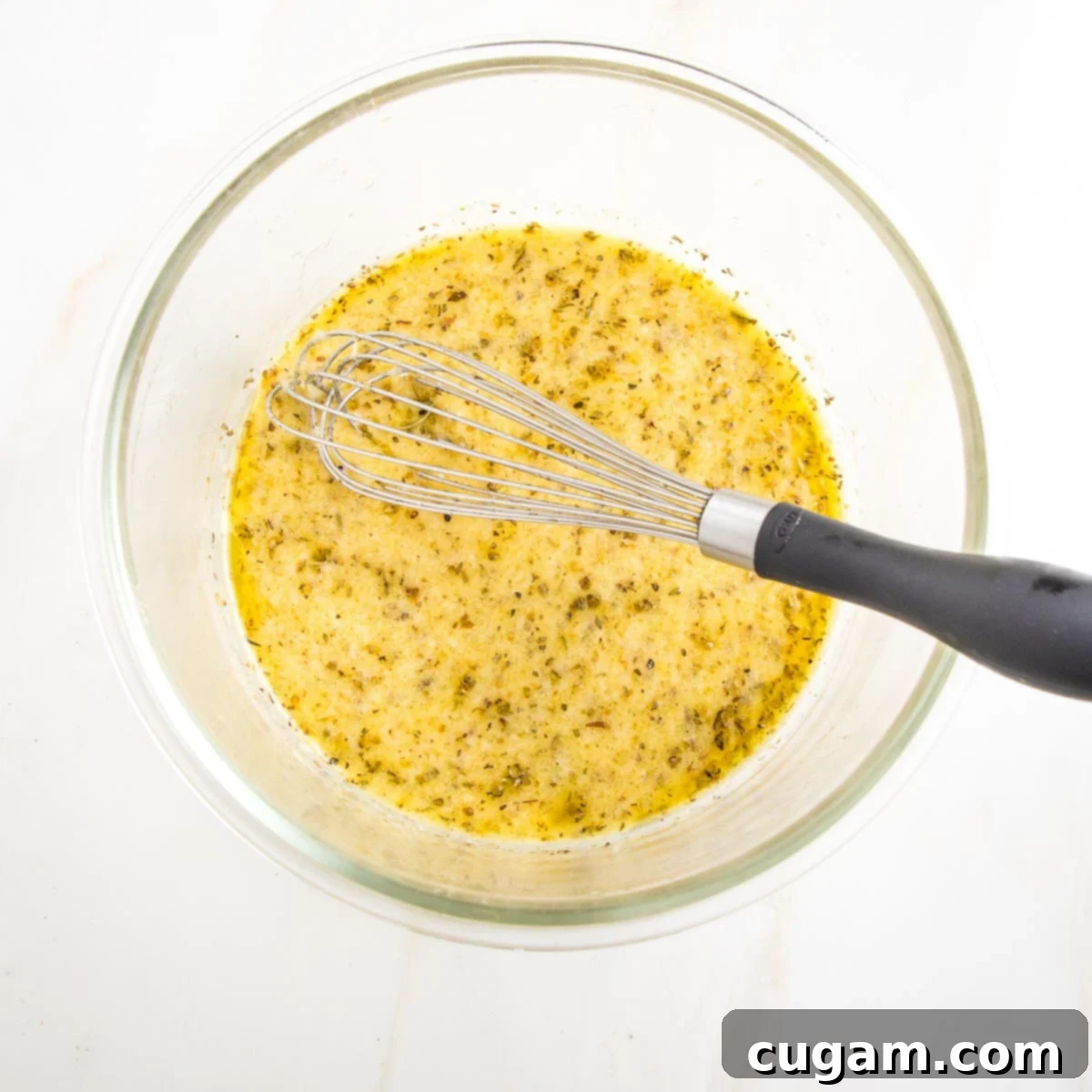 Glass bowl with a whisk, and a mustard, lemon herb mixture.