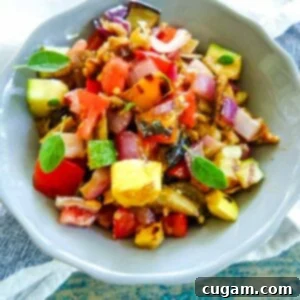 Close-up of a vibrant bowl of diced grilled summer vegetables mixed into a ratatouille salad, garnished with fresh oregano leaves, ready to be enjoyed.