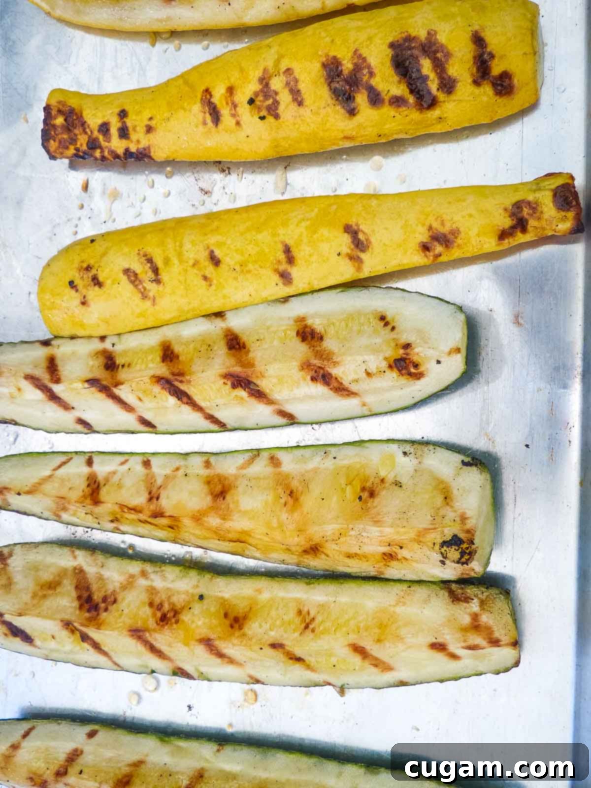 Perfectly grilled slices of bell pepper and red onion being removed from the grill with tongs and placed onto a wooden cutting board.