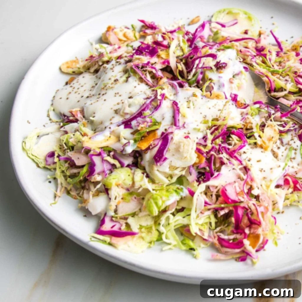 A close-up of a white plate filled with shredded Brussels sprouts and cabbage salad, generously drizzled with creamy dairy-free dressing and sprinkled with toasted nuts and seeds, ready to be enjoyed.