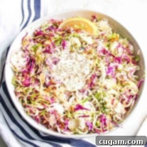 A large white bowl brimming with vibrant Brussels sprouts slaw, featuring colorful red cabbage, finely shredded Brussels sprouts, a medley of various nuts and seeds, a bright lemon wedge, and a generous drizzle of creamy vegan dressing, ready to be served.