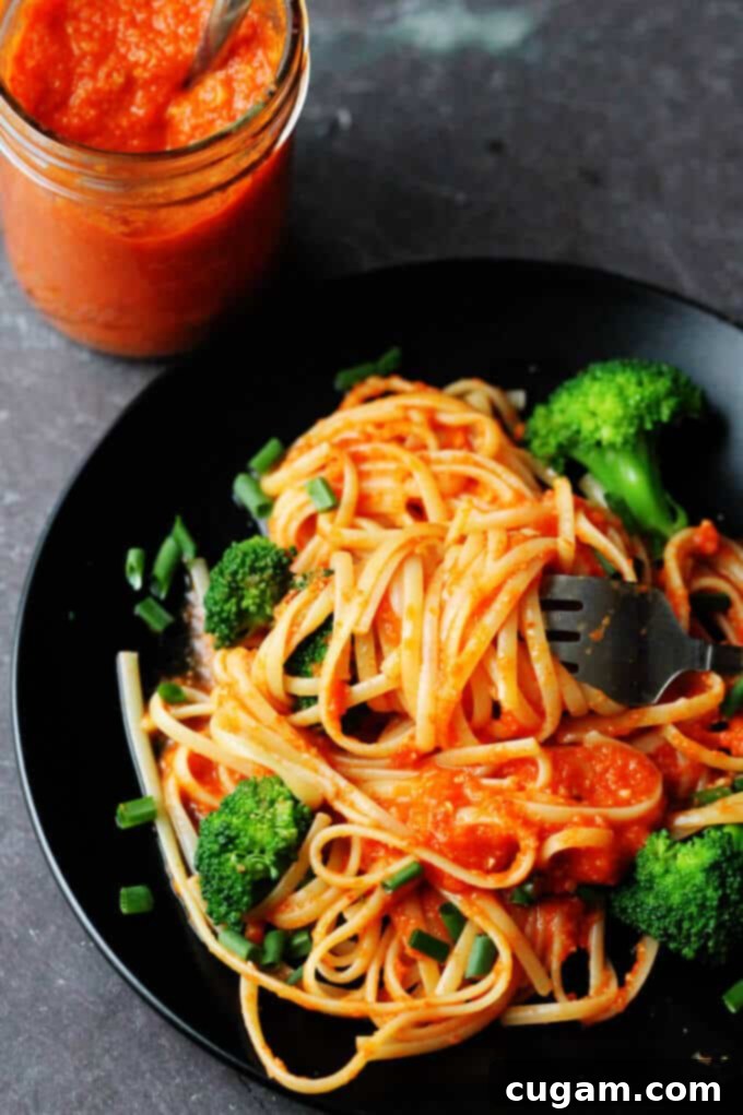 Linguine with vibrant green broccoli florets generously coated in rich, red Romesco sauce, served in a white bowl.