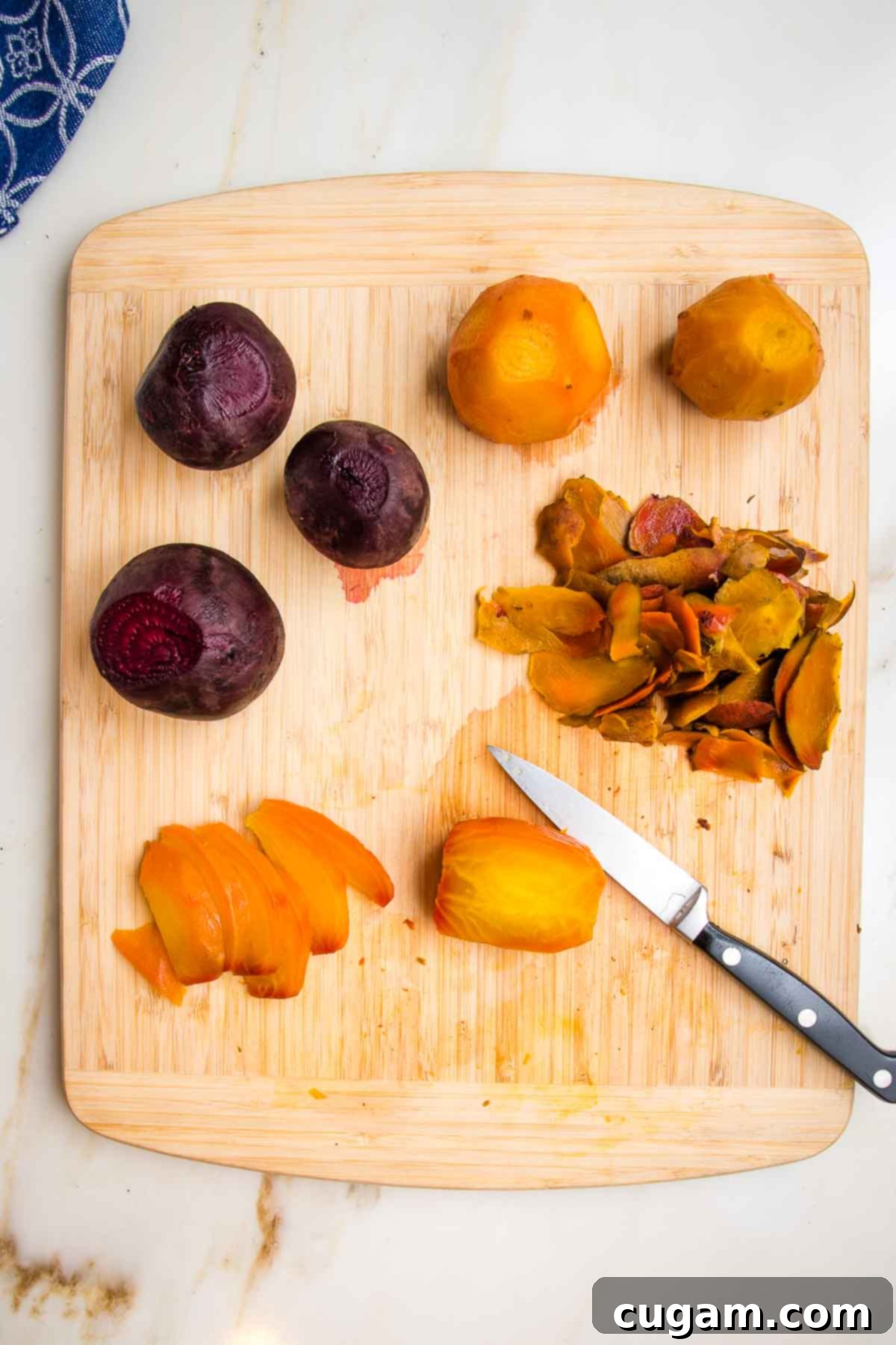 Roasted whole golden beets and red beets, peeled and now being cut into wedges with a paring knife, on a wooden cutting board to make into beet salad. 