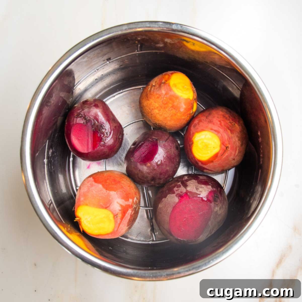 Whole beets, trimmed and ready for cooking, neatly arranged in an Instant Pot bowl on a rack with 1" of water.