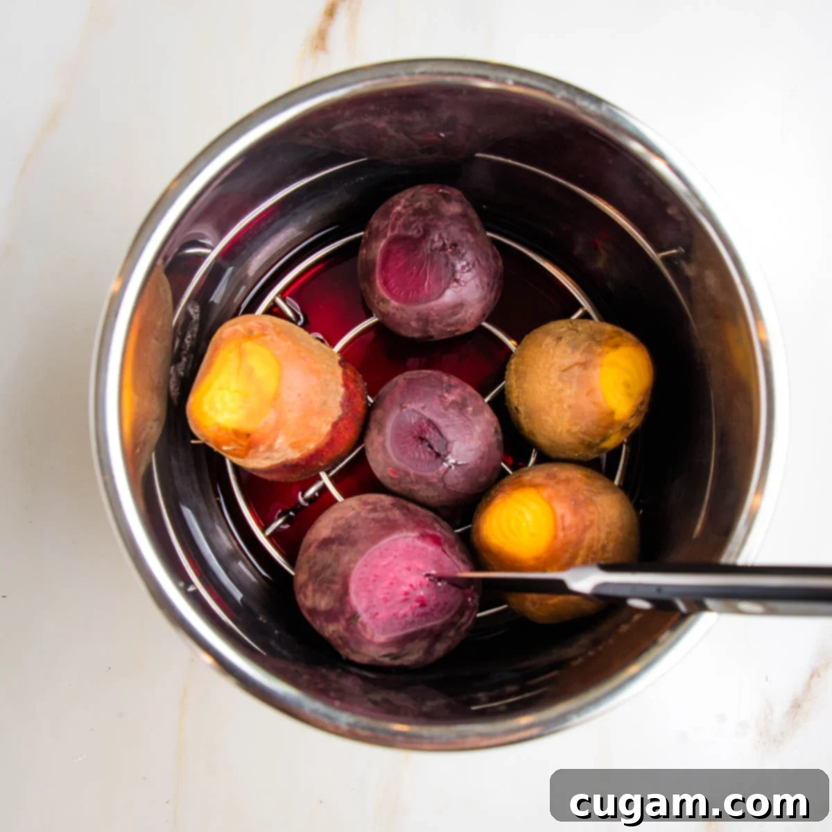 Cooked beets, 3 red, 3 golden, in an instant pot on a rack. Colored water below. Paring knife in one of the beets. 