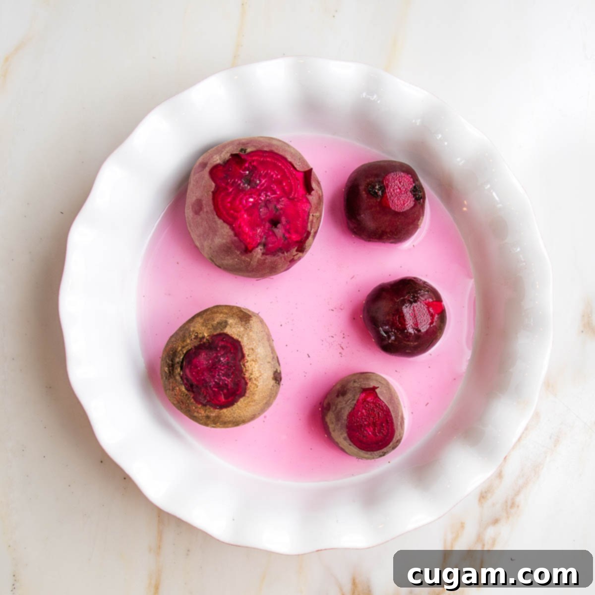 Whole red beets arranged in a pie plate with ¼" water, ready for oven roasting.