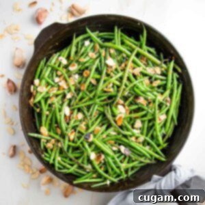 Effortless Green Beans with Toasted Almonds 11 Cast iron pan filled with green beans almondine. There are almond slices, cloves of garlic and crushed red pepper scattered around the pan and a grey napkin tied around the cast iron handle.