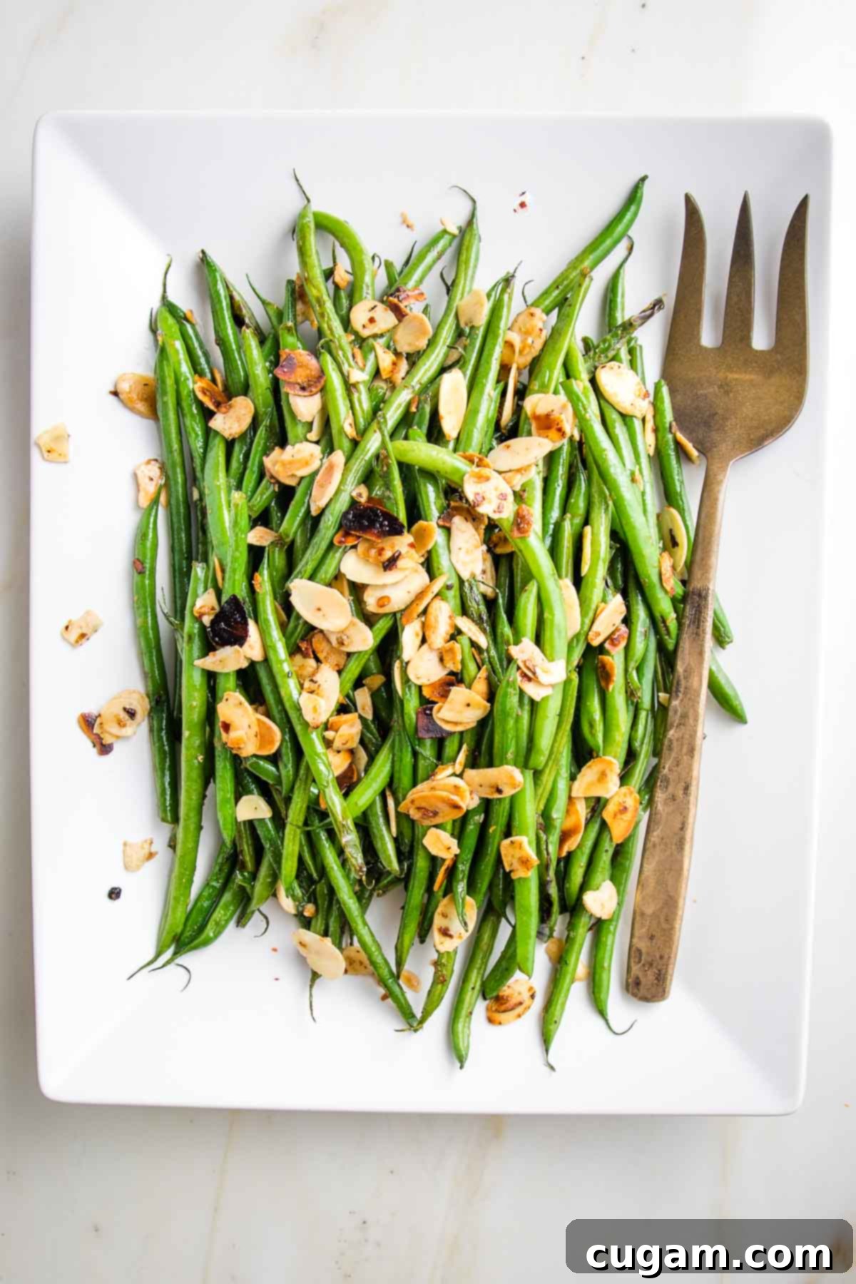 Effortless Green Beans with Toasted Almonds 10 Bright green string beans loaded with sliced almonds and crushed red pepper with a bronze colored serving fork.
