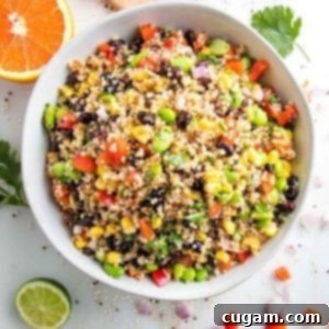 A close-up photograph of a large white bowl filled with a colorful and inviting Southwest Quinoa Salad. The salad is a vibrant mix of fluffy quinoa, diced red bell peppers, bright green edamame, dark black beans, sweet yellow corn, and fresh chopped cilantro. Around the bowl, there’s a half-cut orange, a half-cut lime, and fresh cilantro leaves, emphasizing the fresh, zesty ingredients. This image perfectly captures the appeal of a healthy, plant-based meal.