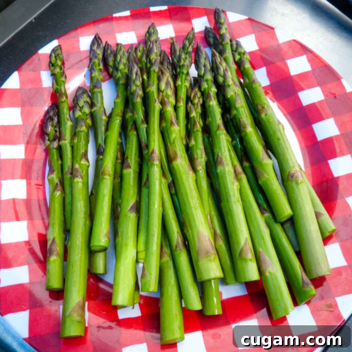 Close-up of freshly trimmed asparagus spears, ready for grilling, artfully arranged on a red checkered plate.