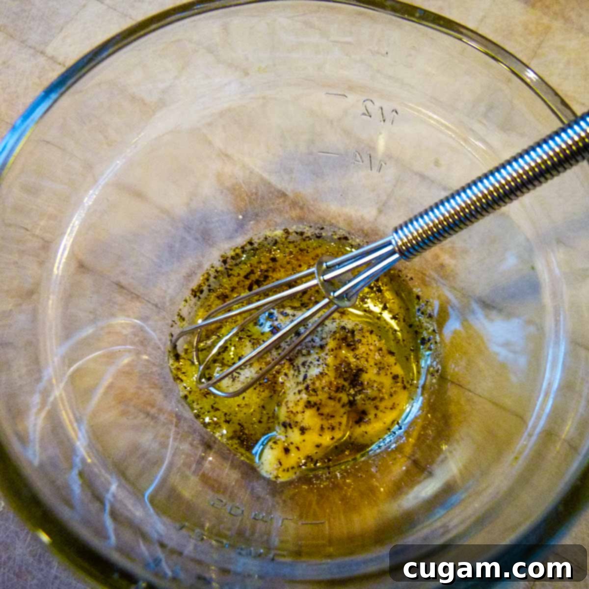 Small bowl containing Dijon mustard, olive oil, lemon juice, salt, pepper, and a teaspoon of water, being whisked vigorously.