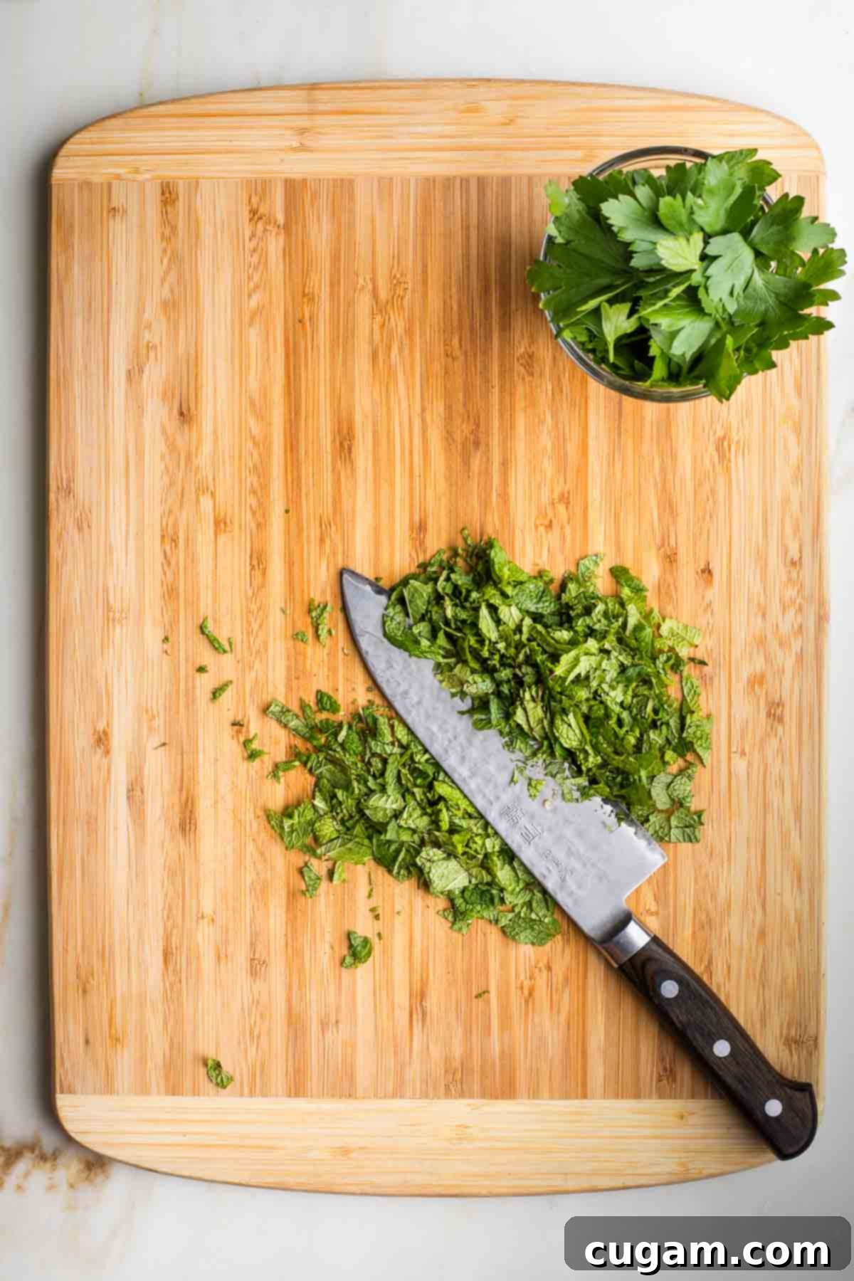Stack of fresh mint leaves being sliced thin and a small dish with fresh parsley leaves.