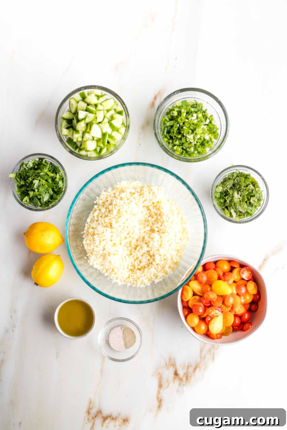 Large bowl of riced parsnips, surrounded by small bowls of chopped ingredients plus two lemons and dish of olive oil.