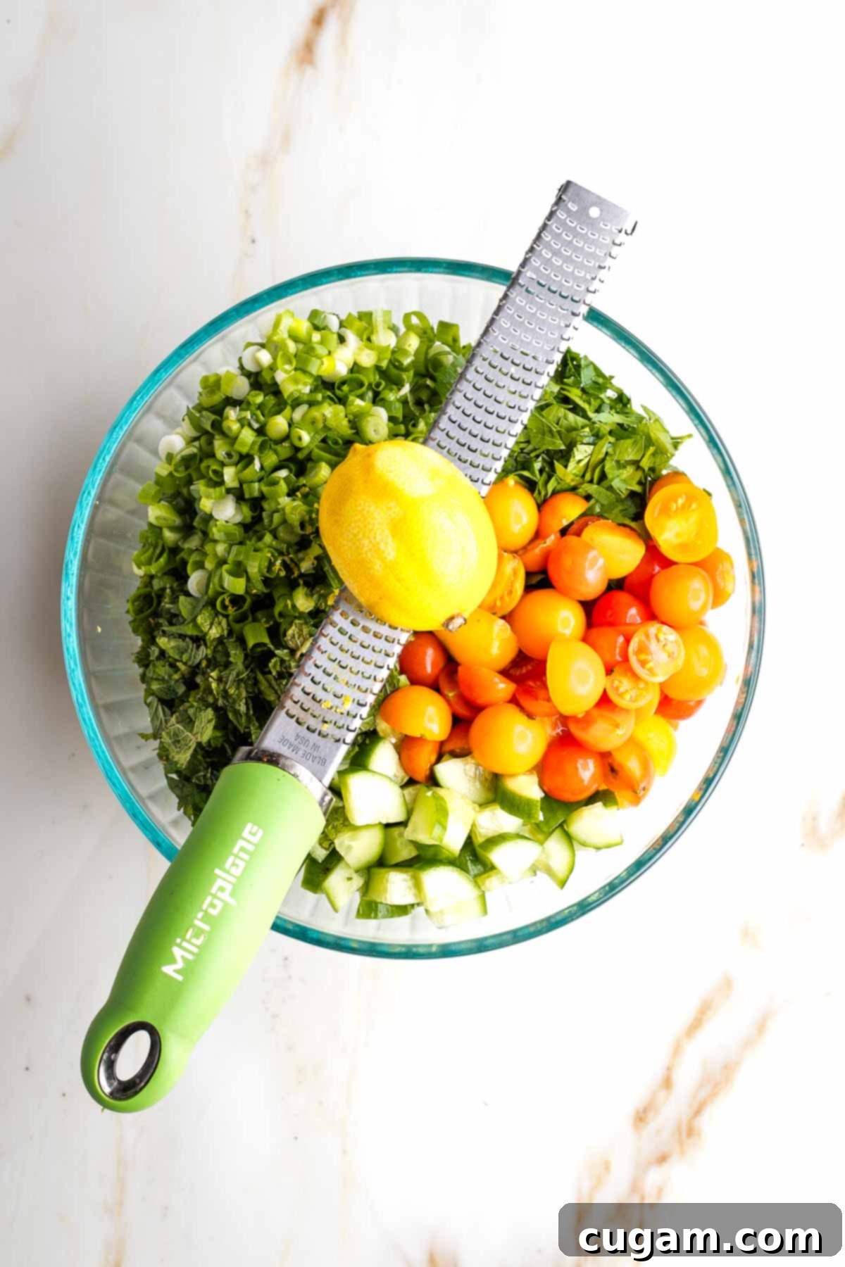 Zesting a lemon over a large bowl filled with chopped veggies and tomatoes.