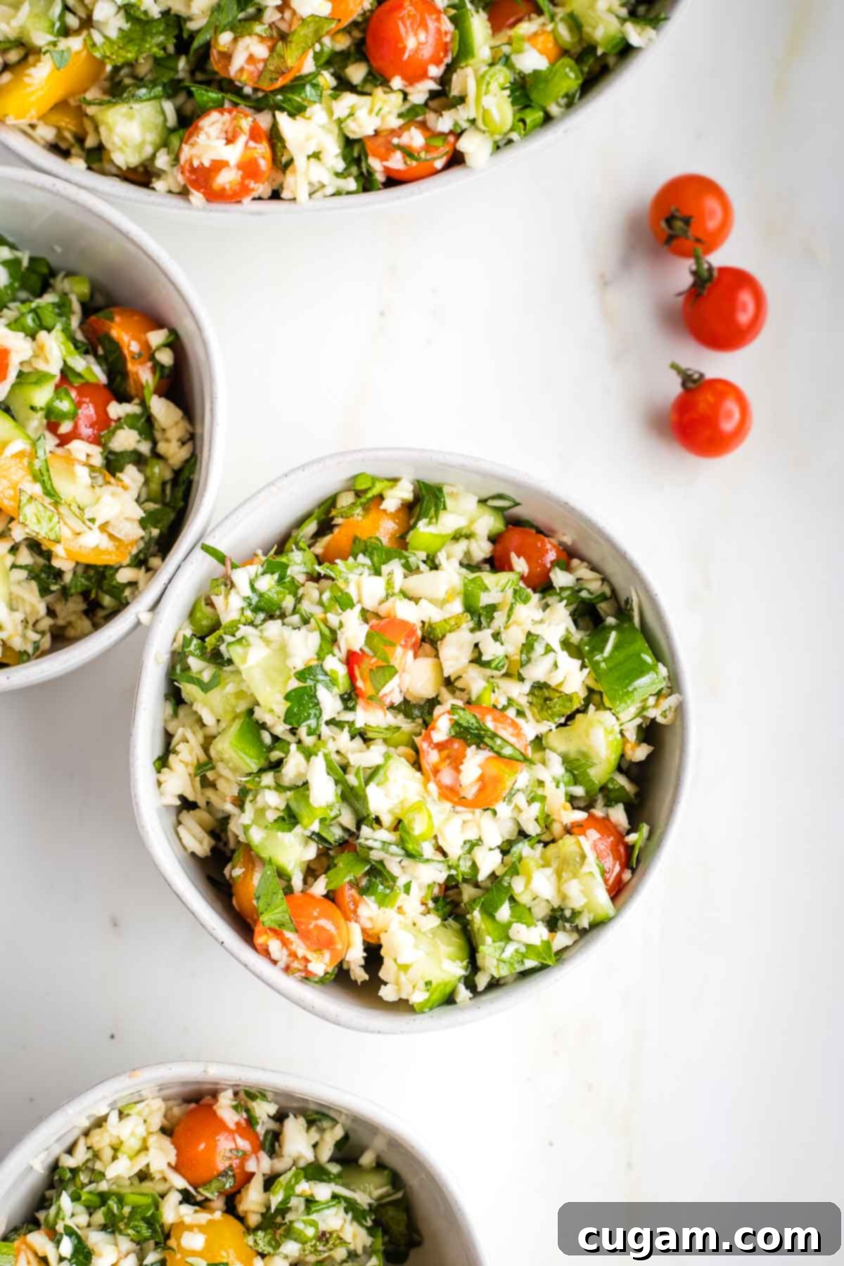 Small bowls filled with colorful tabbouleh and three small cherry tomatoes on the counter.
