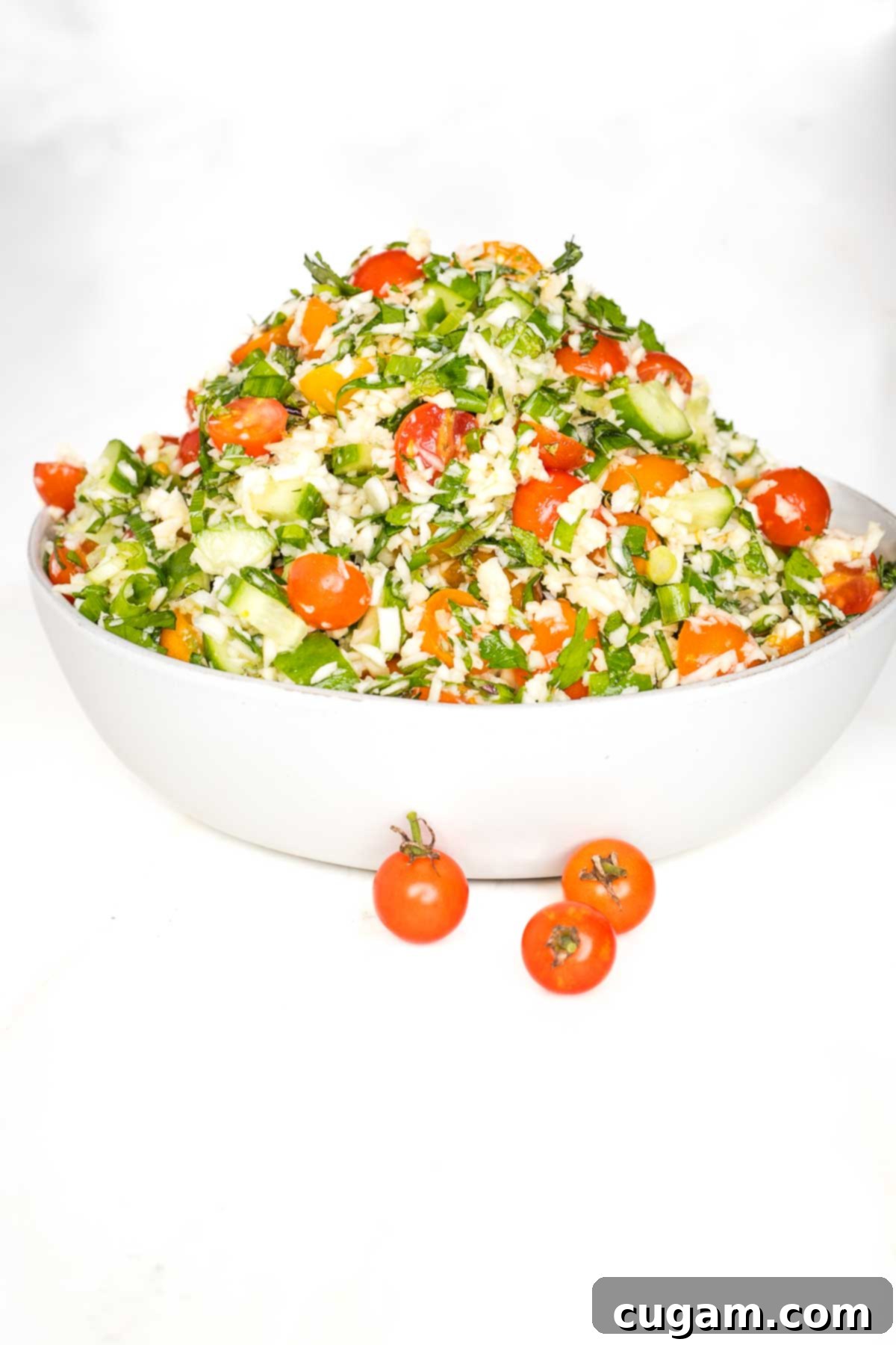 White bowl piled high with tabbouleh that's loaded with fresh tomatoes and cucumbers, lots of fresh herbs, scallions and riced parsnips.