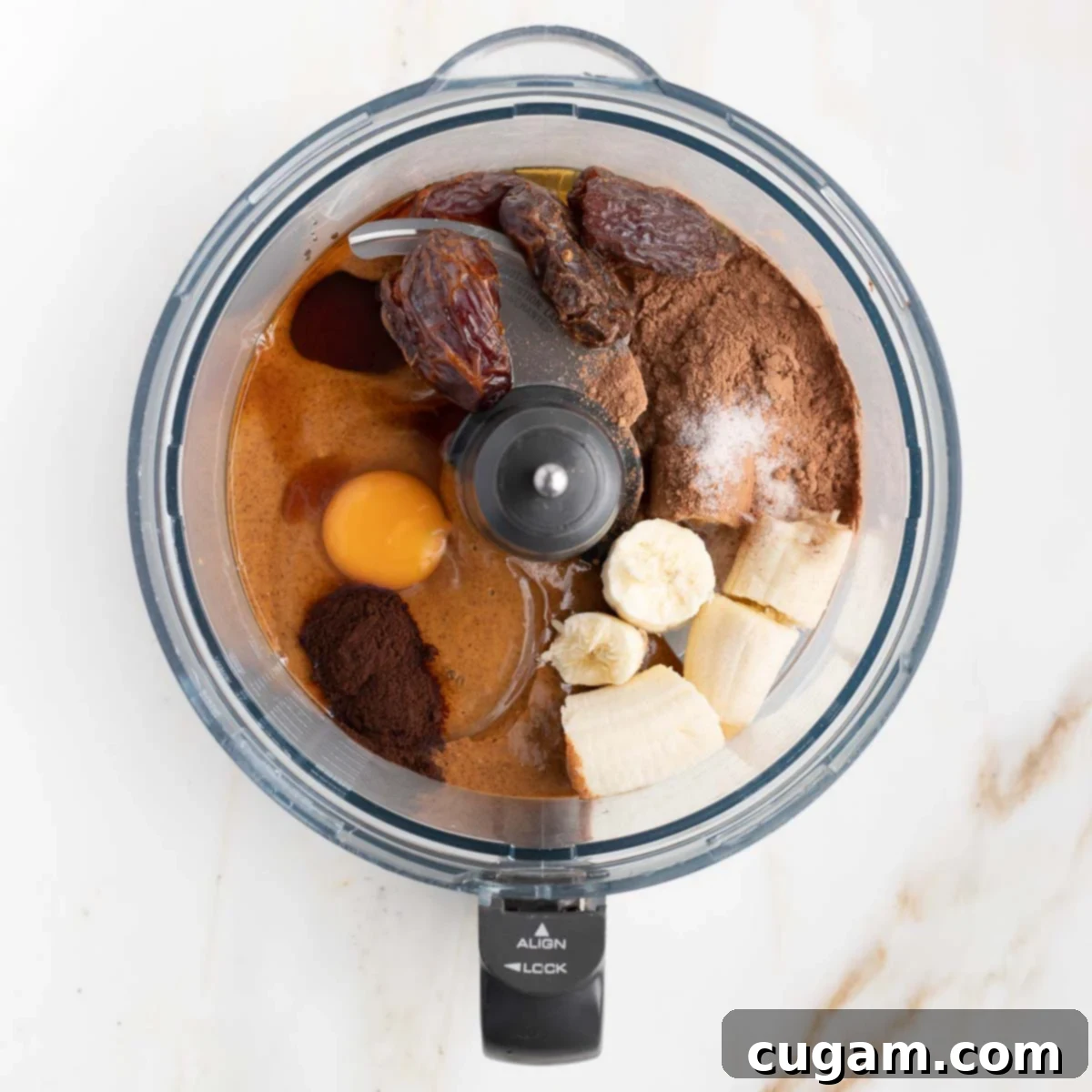 Decadent Double Chocolate Zucchini Muffins 6 Key wet and dry ingredients (banana, egg, cacao powder, dates) are added to a food processor bowl for blending.