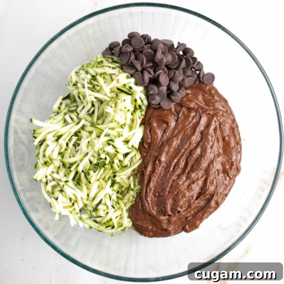 Decadent Double Chocolate Zucchini Muffins 8 The smooth chocolate muffin batter, dark chocolate chips, and shredded zucchini are combined in a large glass mixing bowl.