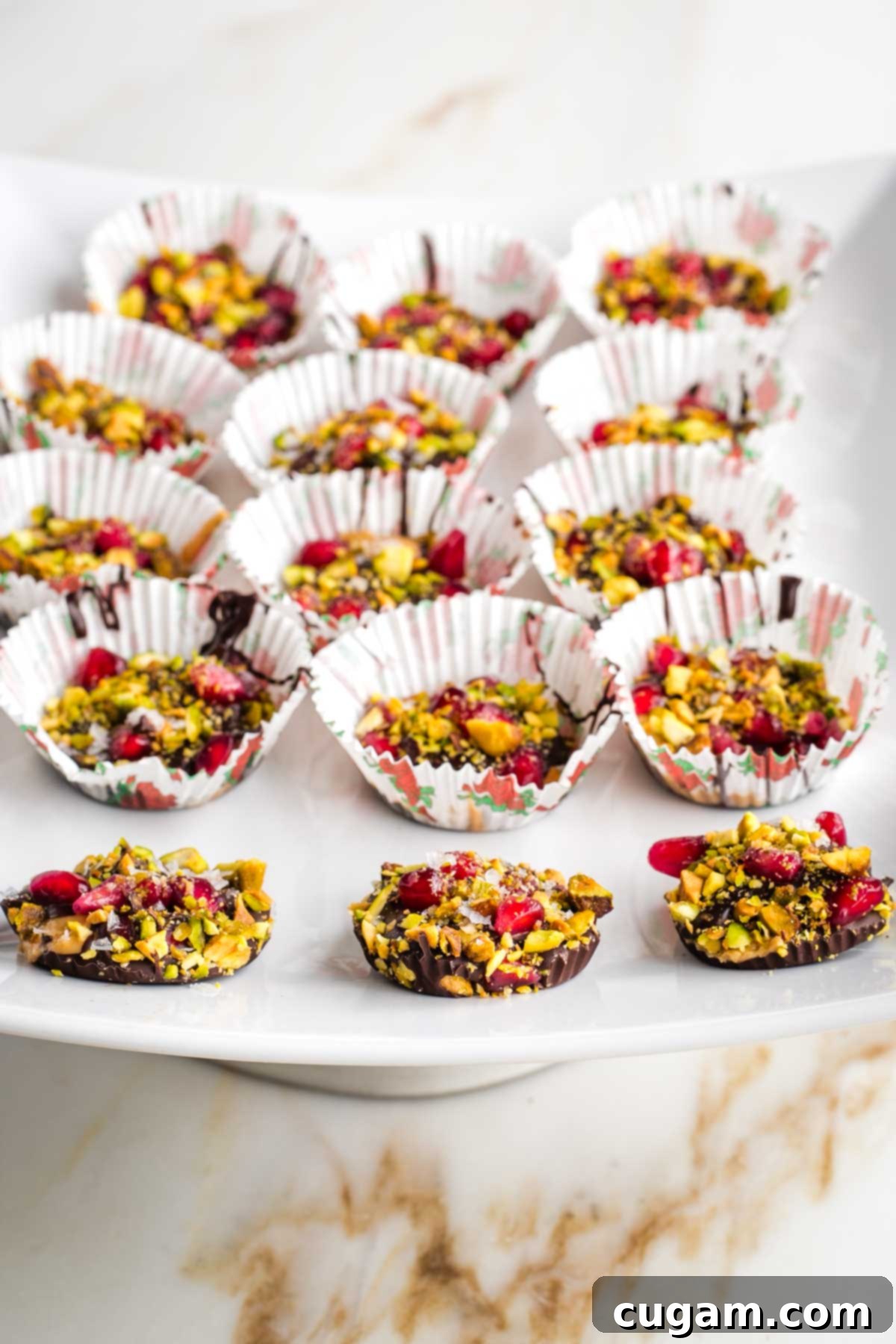 Chocolate peanut butter cups with pistachios and pomegranate seeds, some out of their wrappers.