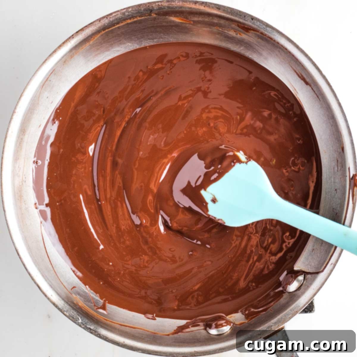 Melted chocolate in a skillet with a blue silicone spatula.