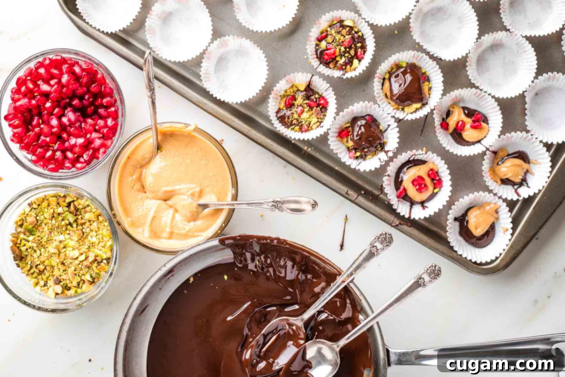 Melted chocolate, chopped pistachios, peanut butter and pistachios in small bowls near a baking sheet with cups of these assorted ingredients. 