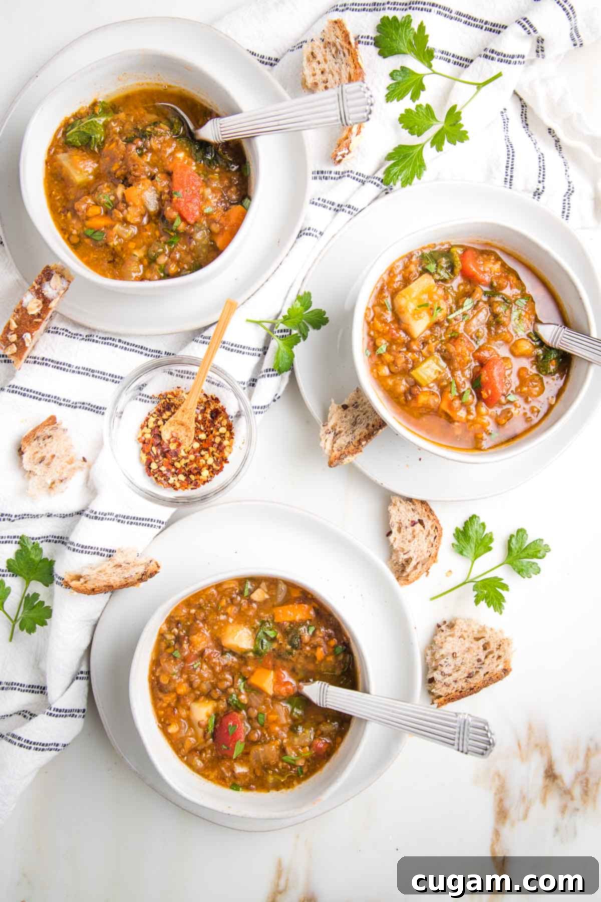 Bowls of chunky lentil soup with crusty bread, fresh parsley and a dish towel. A perfect vegan comfort meal.