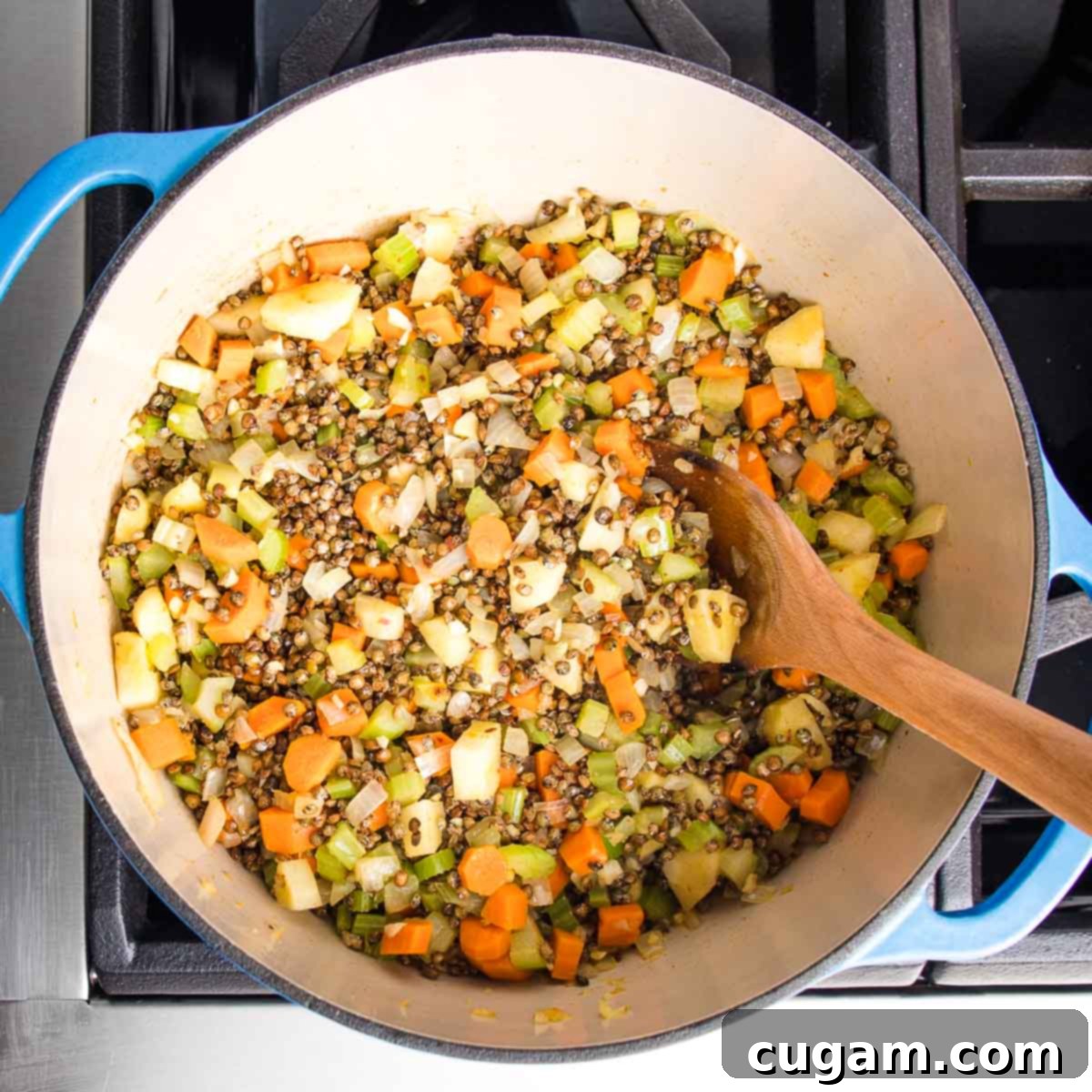 Lentils and chopped veggies in a dutch oven with wooden spoon stirring, ensuring even distribution of flavors.