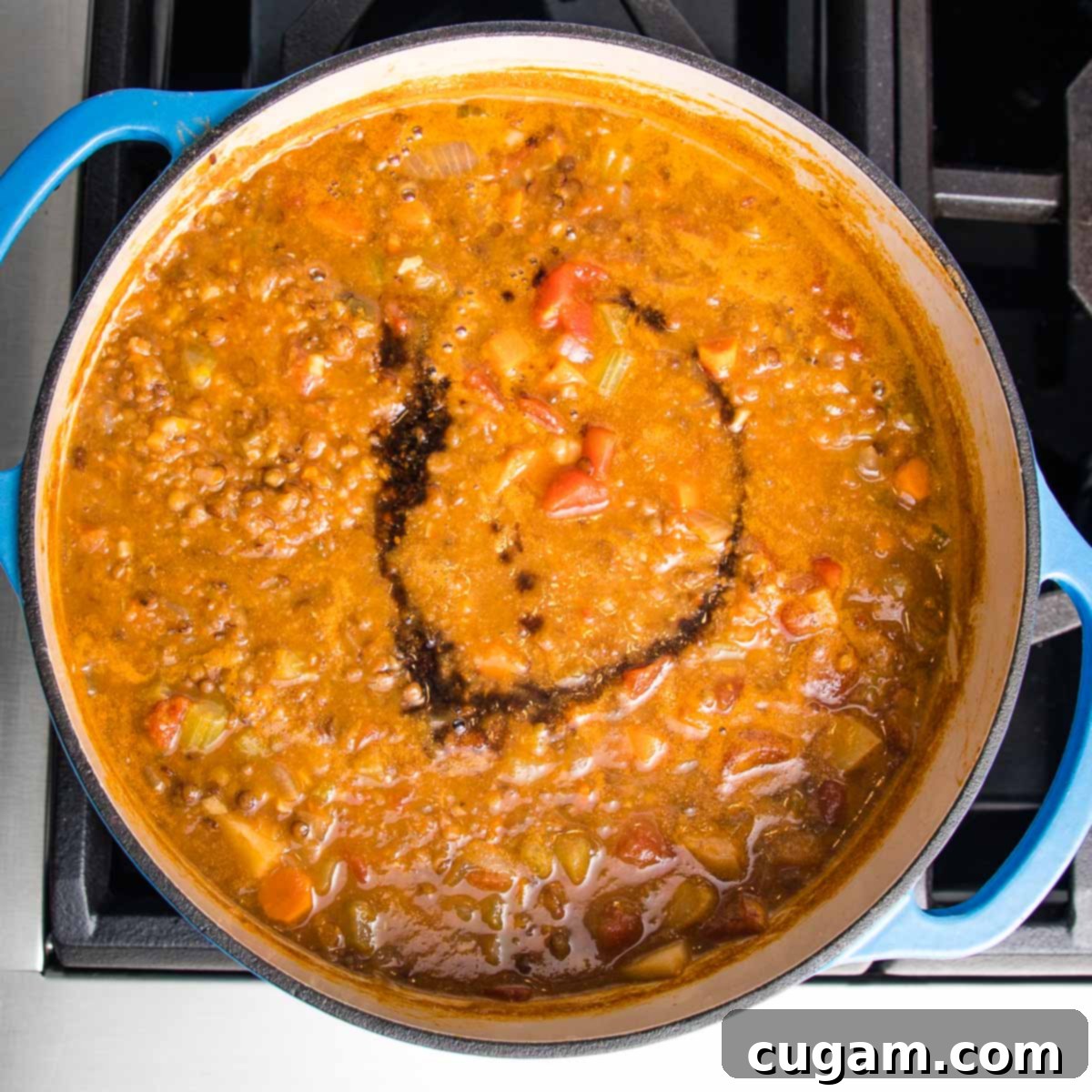 Blended lentil soup in a blue dutch oven, with a swirl of balsamic on top, showcasing the smooth and chunky textures combined.
