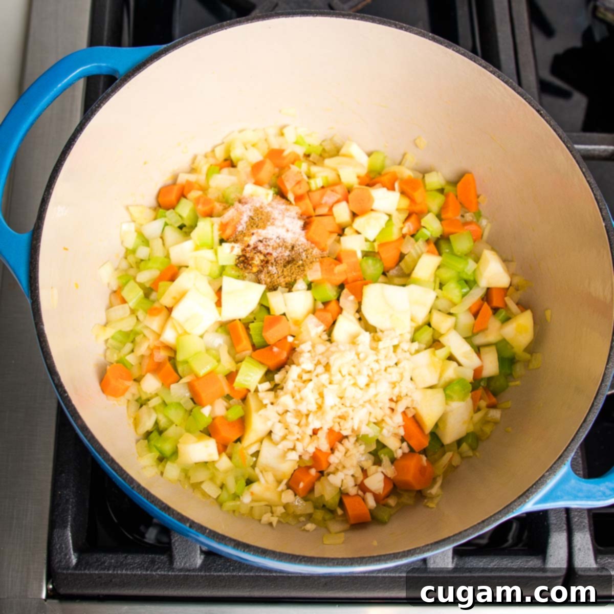 Minced garlic and spices being stirred into softened vegetables in a dutch oven, creating an aromatic base for the soup.