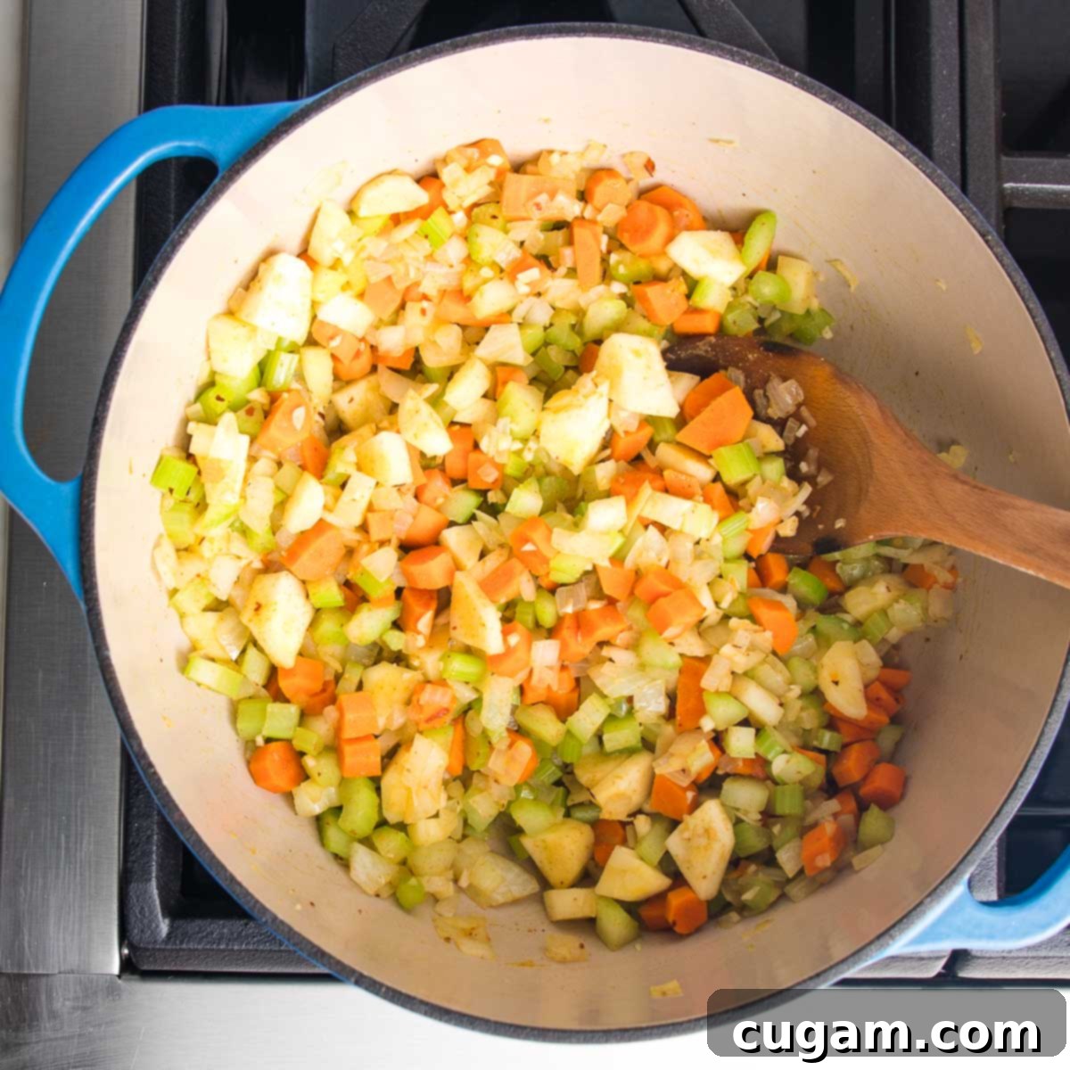 Dutch oven filled with chopped carrots, parsnips, celery and onions, stirred with a wooden spoon, now infused with garlic and spices.