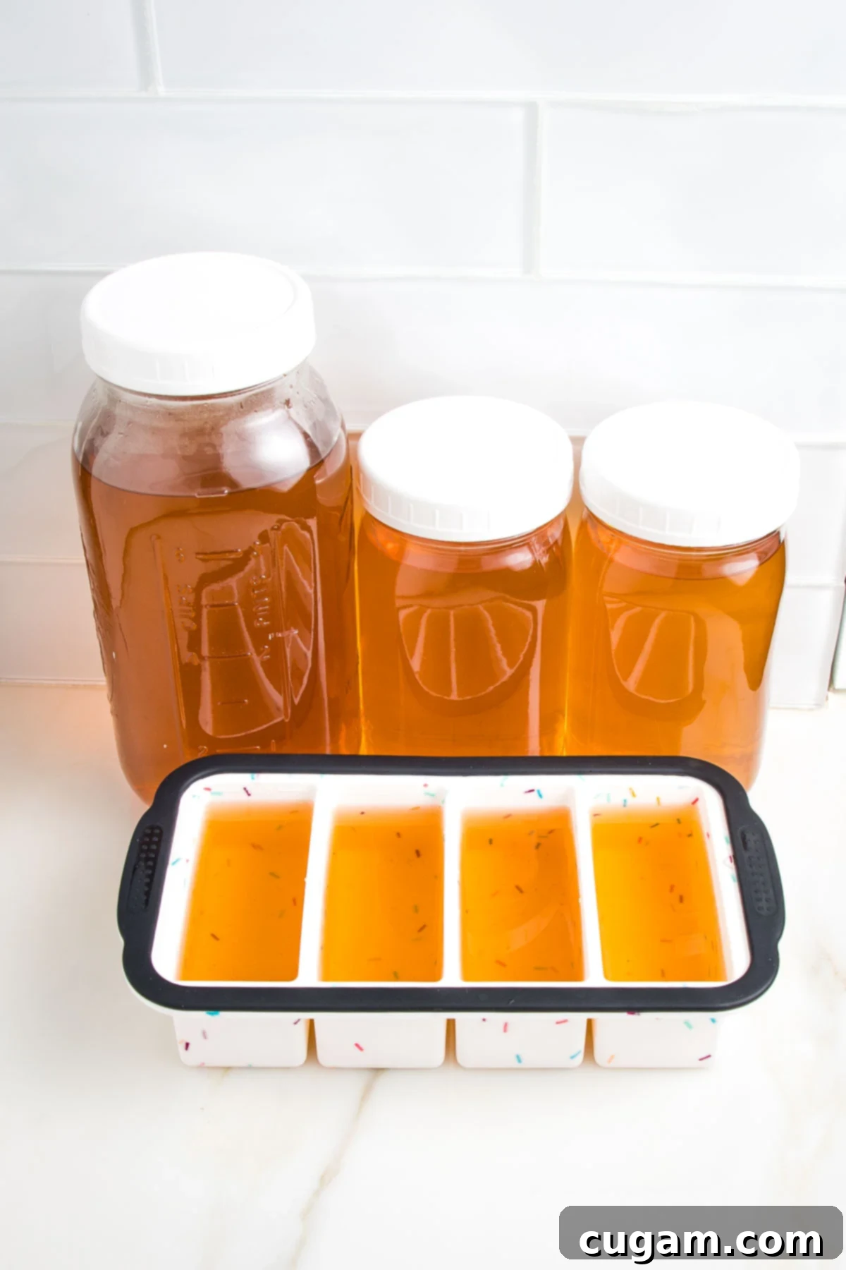 Different sized glass mason jars plus silicone ice cube trays filled with golden colored stock, ready for the freezer.