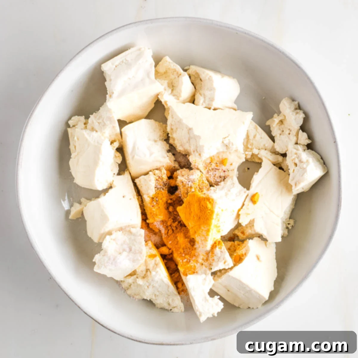 Plant-Powered Tofu Quinoa Stir-Fry 6 Torn pieces of firm tofu in a bowl with ground turmeric, salt and pepper, ready to be seasoned.