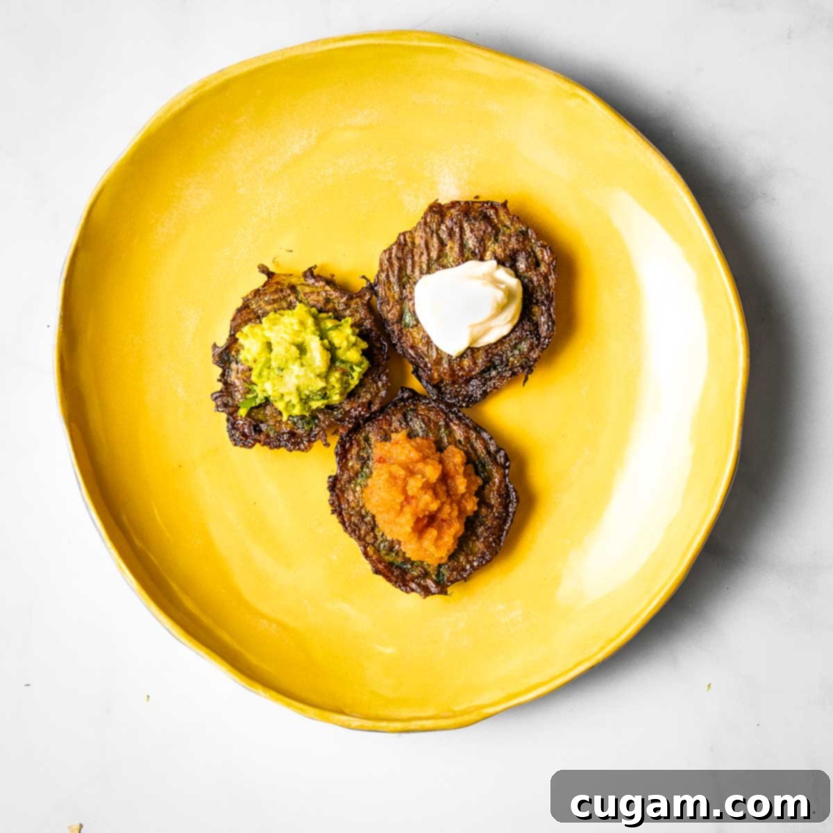 Three latkes with different toppings: applesauce, guacamole and sour cream.