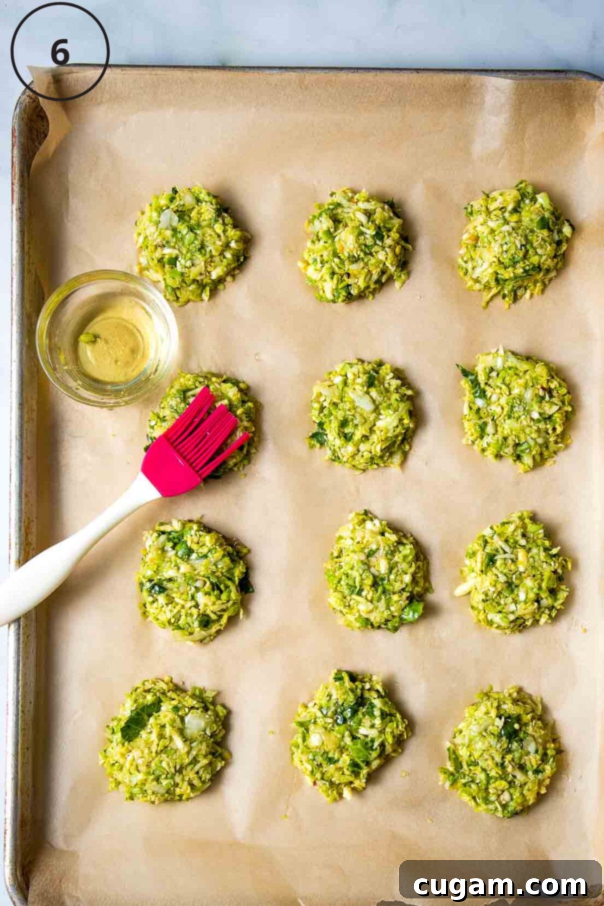 Oil being brushed onto Brussels sprouts latkes on a baking sheet lined with parchment.