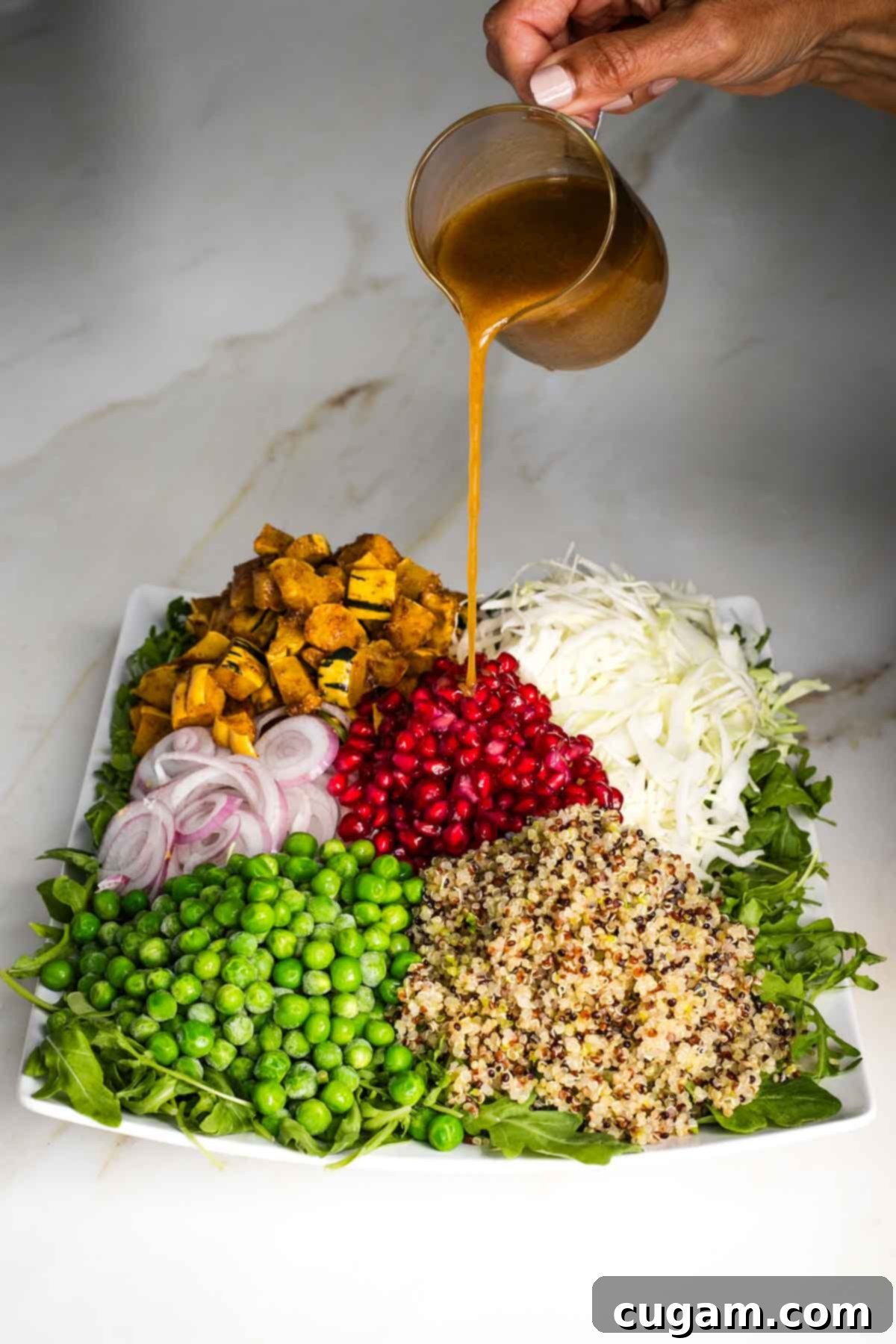 Pouring dressing onto cooked and raw, colorful veggies on a platter of arugula. 