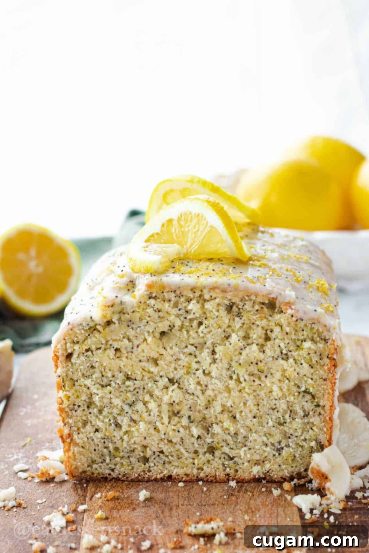 Frosted loaf of lemon zucchini bread with lemon slices and poppyseed on top, resting on wood cutting board.